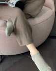 Person wearing brown slipper socks with the ankle area exposed, seated in a pink round chair reading a book.