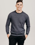 Man wearing a gray sweater and black pants against a plain background