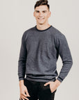 Man wearing a gray sweater and black pants against a plain background
