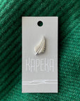 Silver leaf-shaped brooch on a Kapeka card against a green textured background