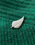 Silver leaf-shaped brooch on a green textured fabric background