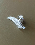 Silver feather-shaped earring on a brown surface