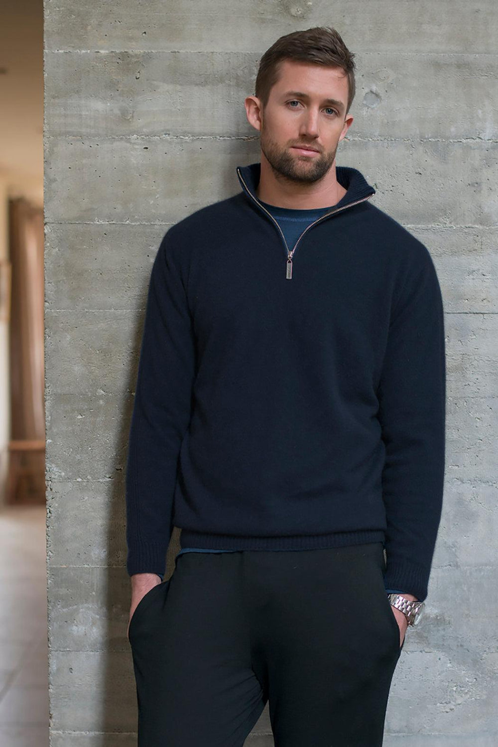 Man wearing a navy blue pullover against a concrete wall