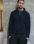 Man wearing a navy blue pullover against a concrete wall