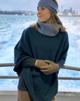 Woman wearing a blue poncho with light blue neckwarmer and head band on ship.