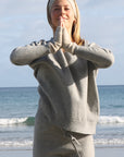 Person in beige outfit standing on a beach with ocean waves in the background