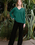 A woman standing outside wearing black merino active pants and a green sweater.
