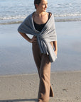 A woman standing on a beach wearing black merino active pants and a light-colored sweater.