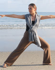 A woman standing on a beach wearing black merino active pants and a light-colored sweater.