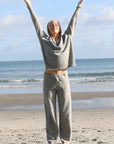 A woman standing on a beach wearing black merino active pants and a light-colored sweater.