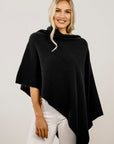 Woman wearing a black merino poncho against a plain background