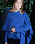 Woman wearing a blue poncho against a dark background with greenery