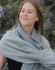 Woman wearing a gray shawl outdoors with rocks and plants in the background