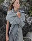 A woman standing outdoors wearing a gray Merinosilk travel wrap that is draped over her shoulders.