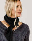 Woman wearing a black scarf and gray sweater against a plain background