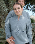 Two people wearing gray sweaters with a snowflake design, standing outdoors near a tree.