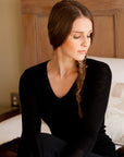 A woman sitting and wearing a long sleeve black merino thermal top with a V-neck.