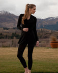 Woman in black outfit standing in a scenic outdoor setting with mountains in the background