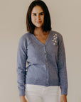 A woman wearing a blue Merinosilk Manuka Cardigan with button-closure, featuring embroidery of Manuka flowers and bees.