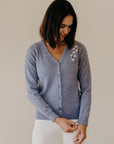Woman wearing a blue cardigan with a floral pattern against a plain background