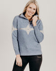 Woman wearing a blue zip sweater with a snow flake pattern on a plain background
