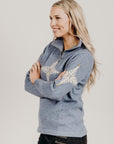 Woman wearing a blue zip sweater with white snow flake patterns on a plain background