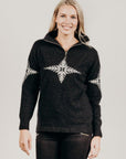 Woman wearing a black zip sweater with a white snowflake design on a plain background