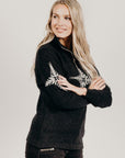 Woman wearing a black zip sweater with white snow flake patterns on a plain background