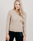 Woman wearing a beige sweater and black pants against a plain background