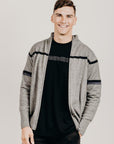 Man wearing a gray zip jacket with black stripes on a plain background