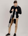 Man wearing a charcoal sweater and plaid scarf against a plain background