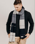 Man wearing a charcoal sweater and plaid scarf against a plain background