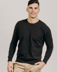 Man wearing a dark color sweater and beige pants against a plain background