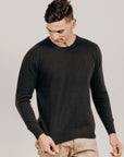 Man wearing a black sweater and beige pants against a plain background