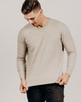 Man wearing a beige sweater and black pants against a plain background