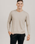 Man wearing a beige sweater and black pants against a plain background