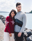 Two people standing on a rocky shoreline waring zip sweater with water in the background