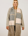 Woman wearing a beige sweater with a scarf on a plain background