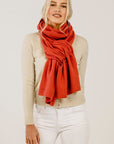 Woman wearing a red scarf, beige sweater, and white pants on a plain background