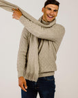 Man wearing a beige sweater and scarf against a plain background