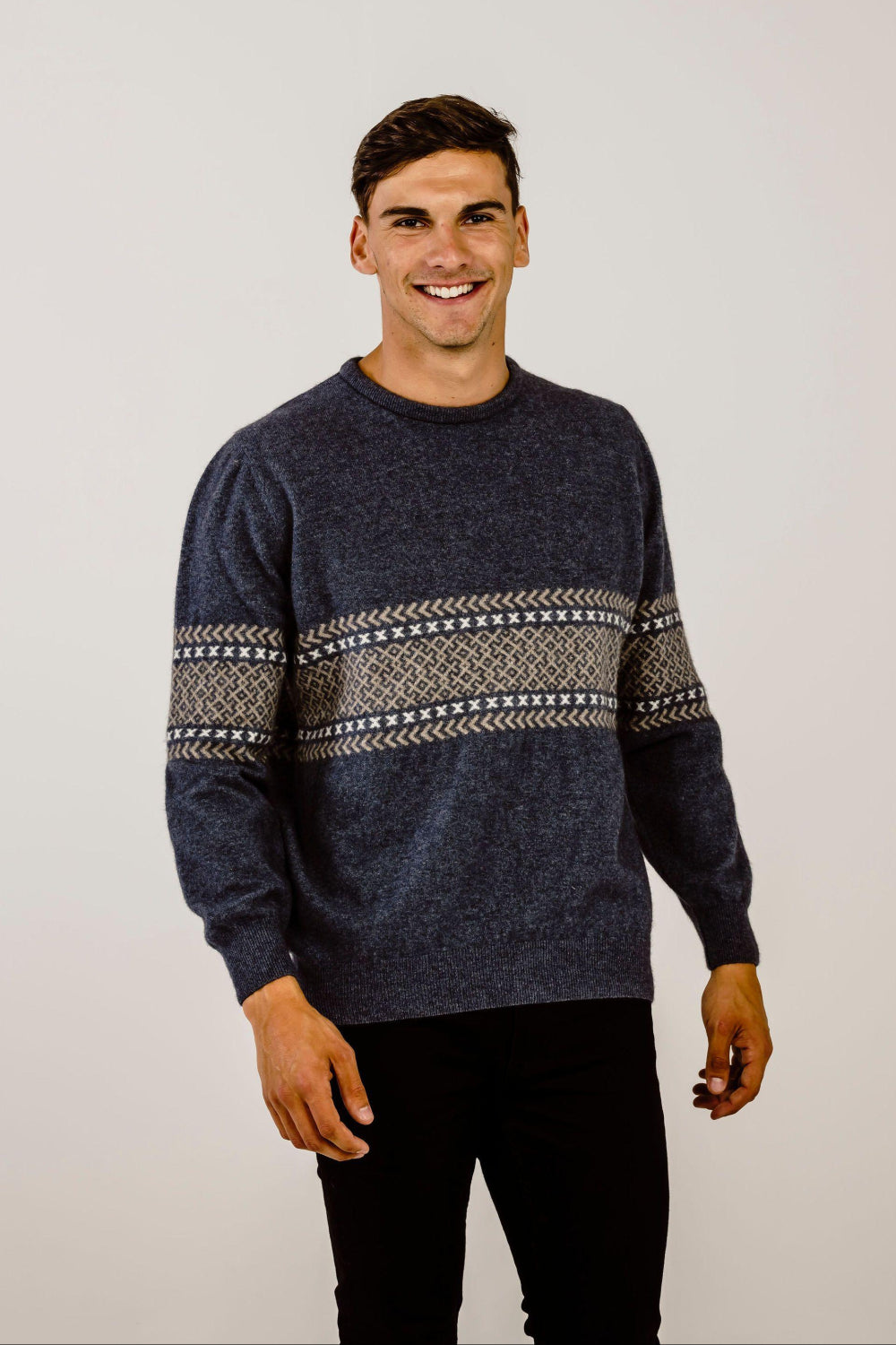 Man wearing a dark blue sweater with a patterned design on a plain background