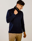 Man wearing a navy sweater and beige pants against a plain background