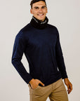 Man wearing a navy turtleneck sweater and beige pants against a plain background
