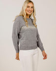 Woman wearing a gray sweater with embellishments on a plain background