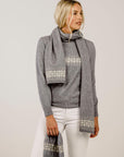 Woman wearing a gray sweater and patterned scarf against a plain background