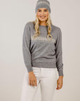 Woman wearing a gray sweater with a patterned beanie on a plain background