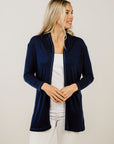 Woman wearing a navy blue cardigan over a white top and pants on a plain background