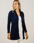 Woman wearing a navy cardigan over a white top and pants on a plain background