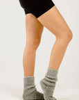 A pair of gray alpaca bed socks worn on human legs, showing the textured cuff.