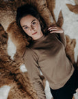Woman in a brown sweater and black shorts lying on a fur rug